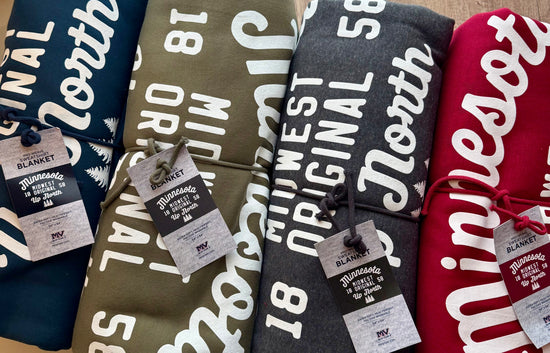 Four blankets with 'Minneapolis' text and tags, displayed against a neutral background.