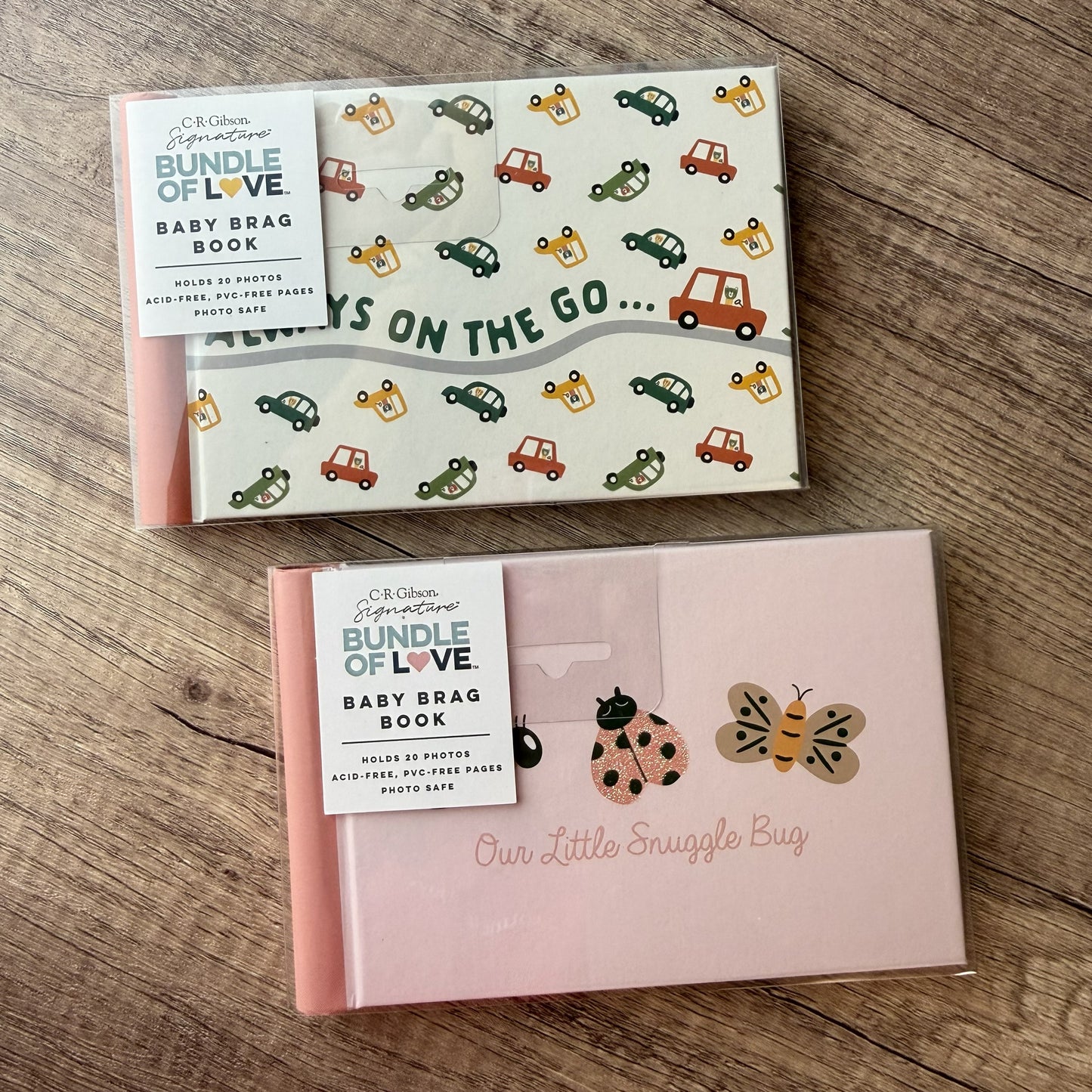 Two boxed baby book sets from C&K Design Studio 'Bundle of Love' displayed on a wooden surface. The top set is white with a colorful pattern of cars and the text 'Always on the Go.