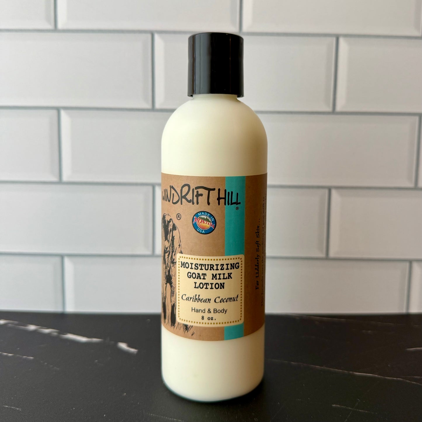 Bottle of Drift Hill moisturizing goat milk lotion on a dark surface with a tiled wall background