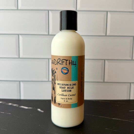 Bottle of Drift Hill moisturizing goat milk lotion on a dark surface with a tiled wall background