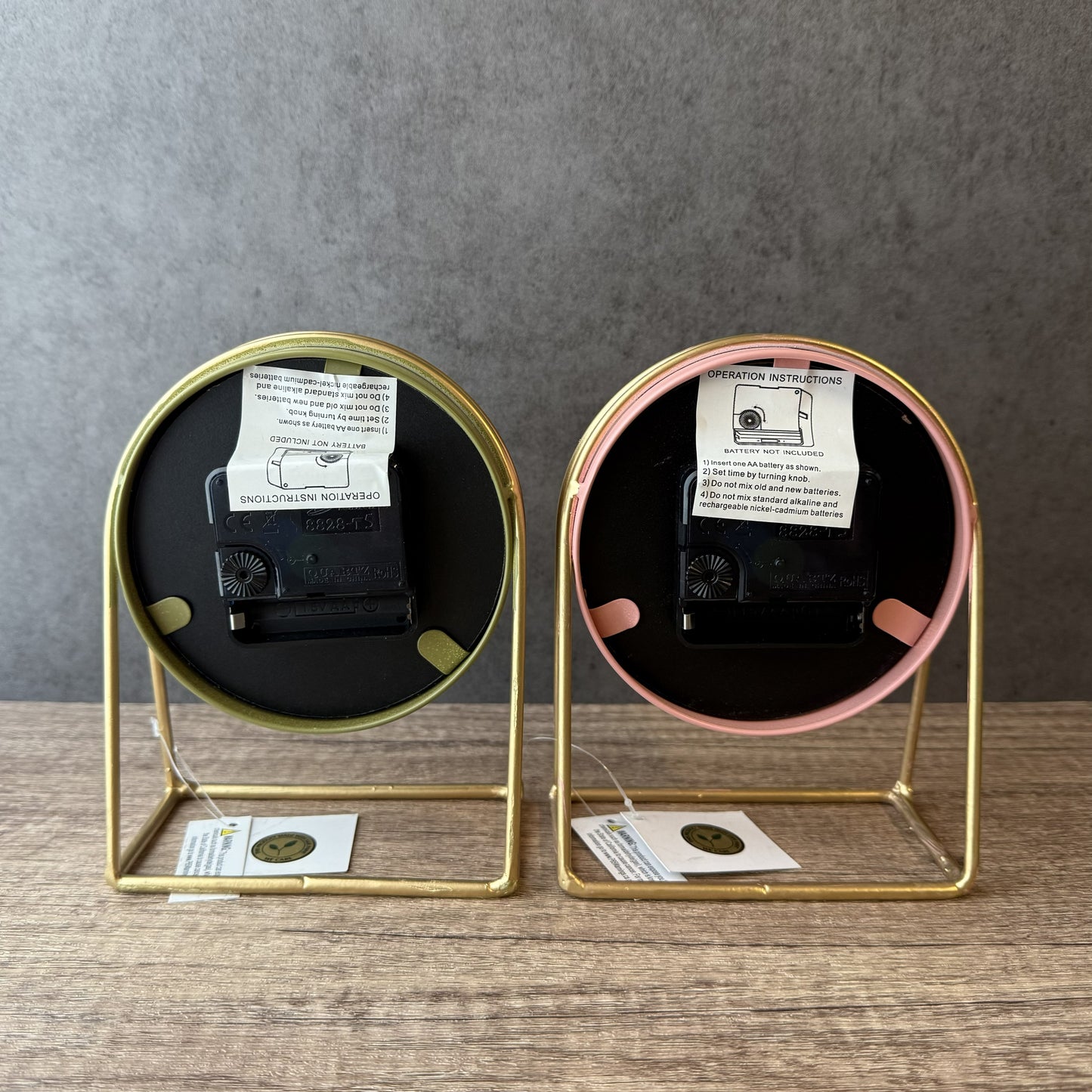 Two small round mirrors with gold frames on a wooden surface against a gray background