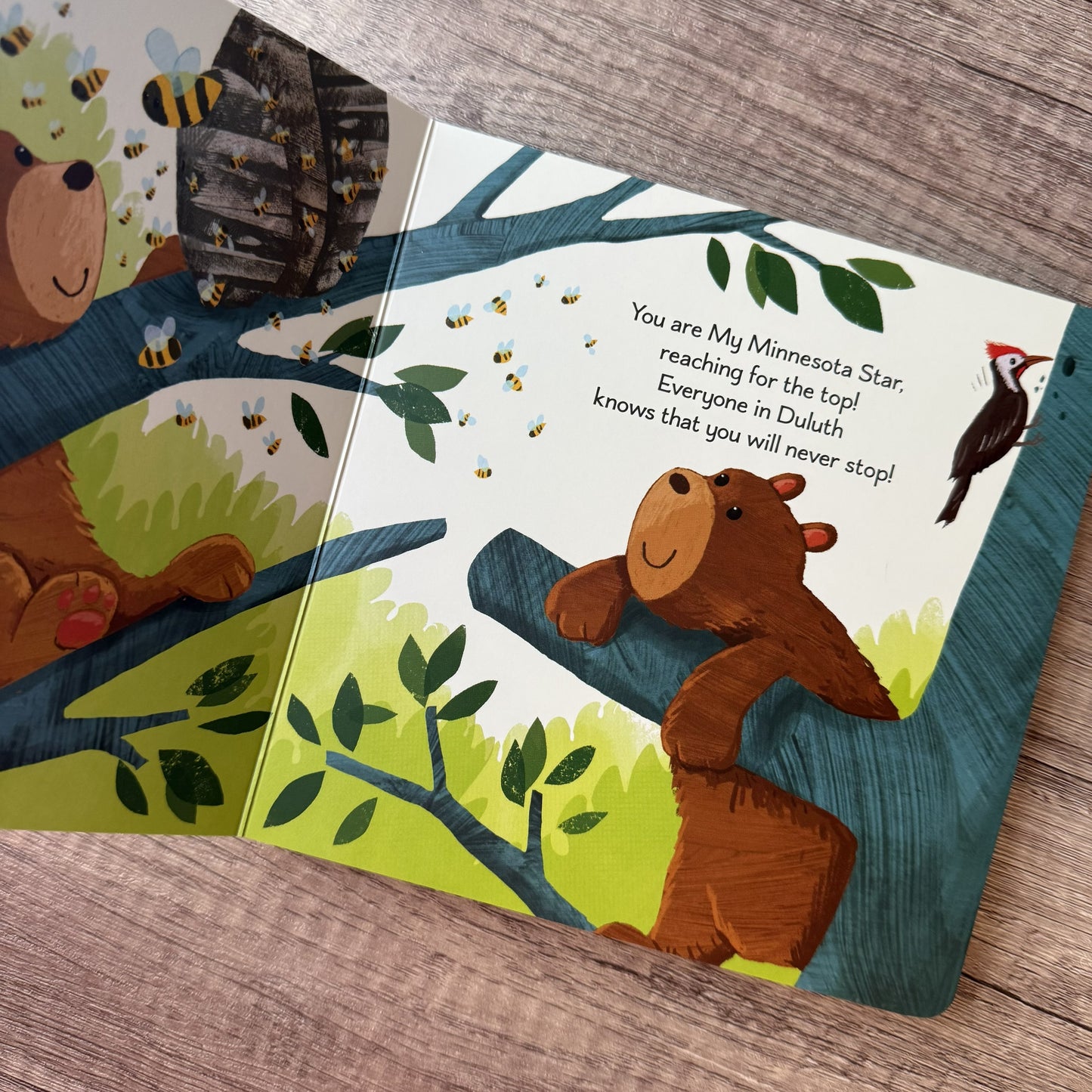 An open children's book lying on a wood surface, showing illustrated forest animals, bees, and text on the pages. The visible subject is the book itself rather than a person or real-life usage scene, so this fits Product/Packaging rather than Lifestyle.