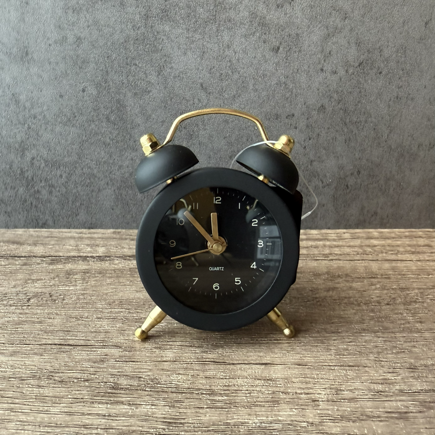 Black alarm clock with gold accents on a wooden surface against a gray wall
