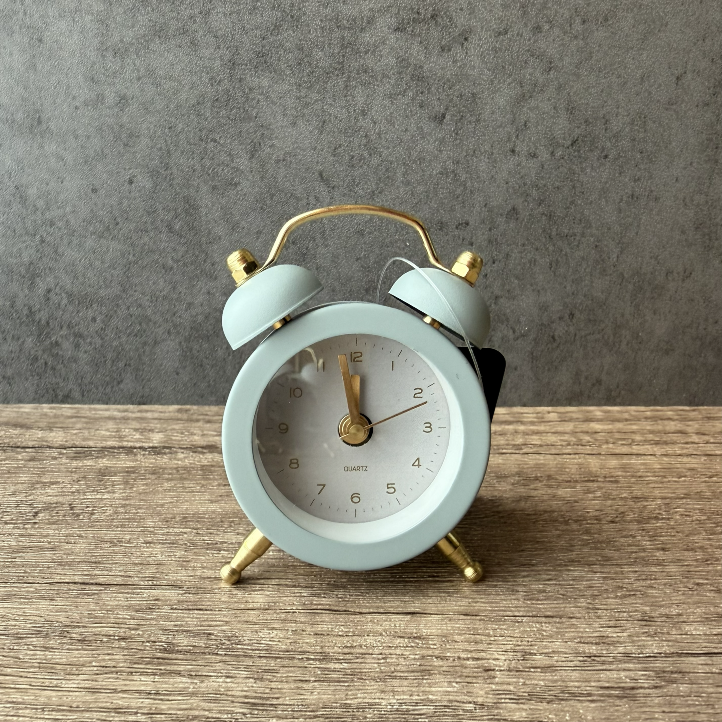 stone grey alarm clock with gold accents on a wooden surface and gray background