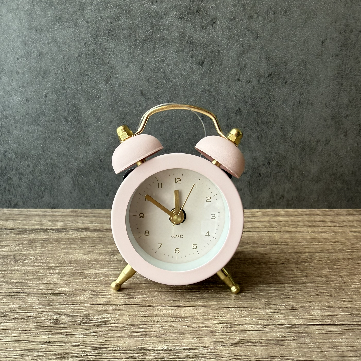 Pink alarm clock with gold accents on a wooden surface and gray background