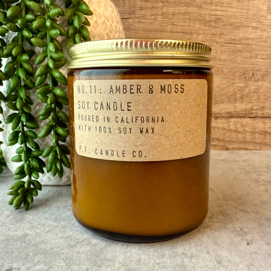 Amber soy candle with a gold lid and label on a neutral background