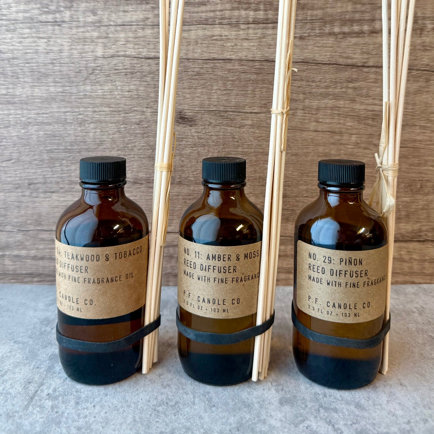 Three brown bottles with labels and wooden reeds on a textured surface.