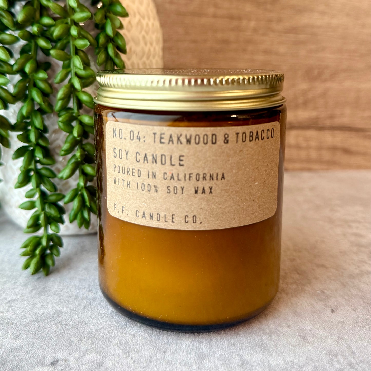 Soy candle with a label on a textured surface next to greenery