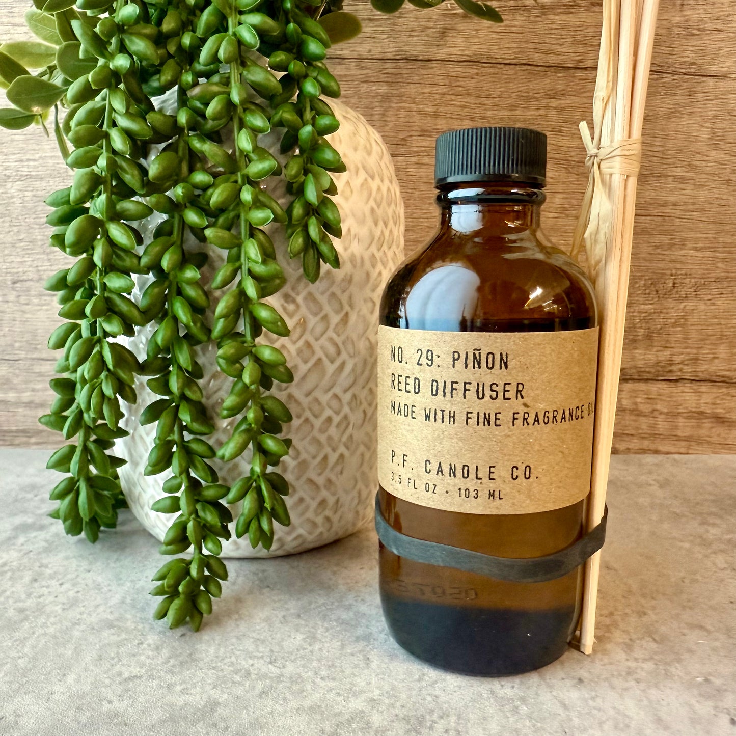 Brown reed diffuser bottle with label next to a green plant on a wooden surface