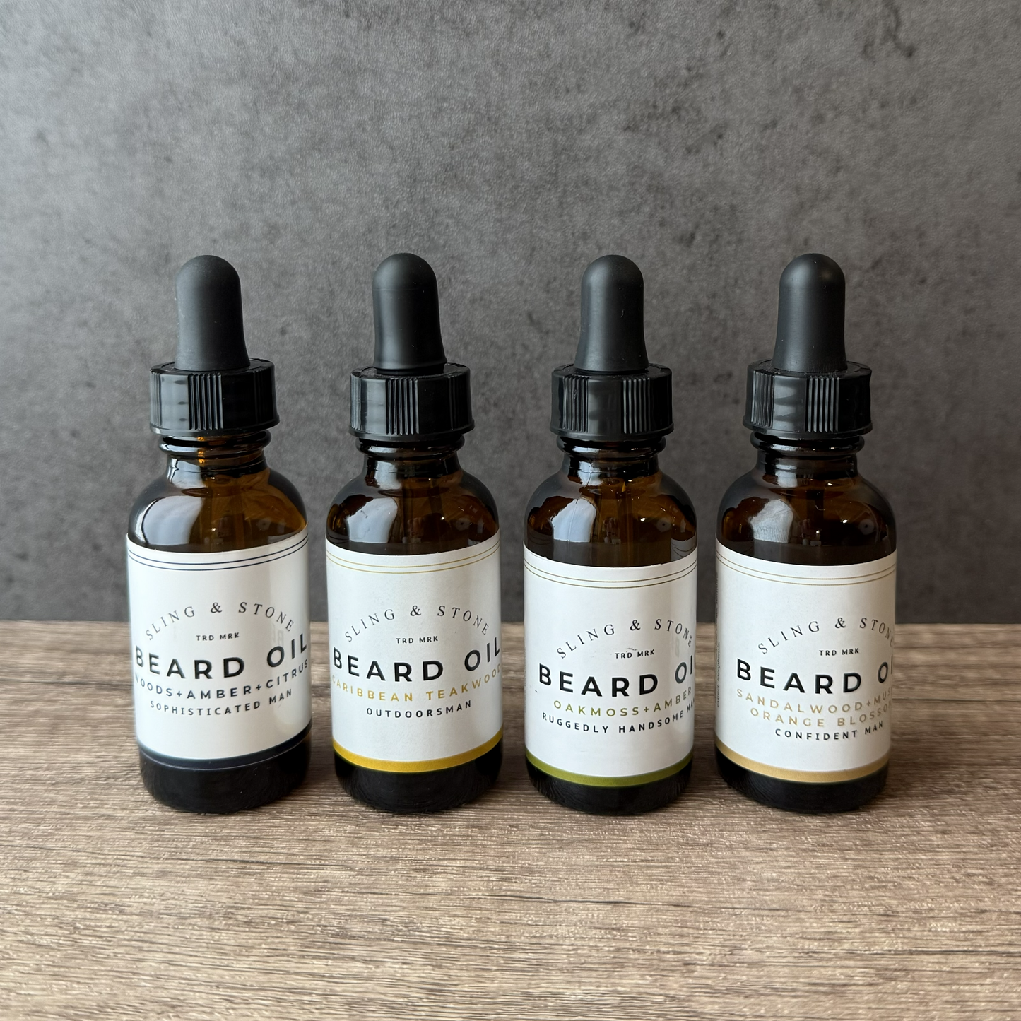 Bottles of Sling & Stone beard oil with dropper on a wooden surface and gray background
