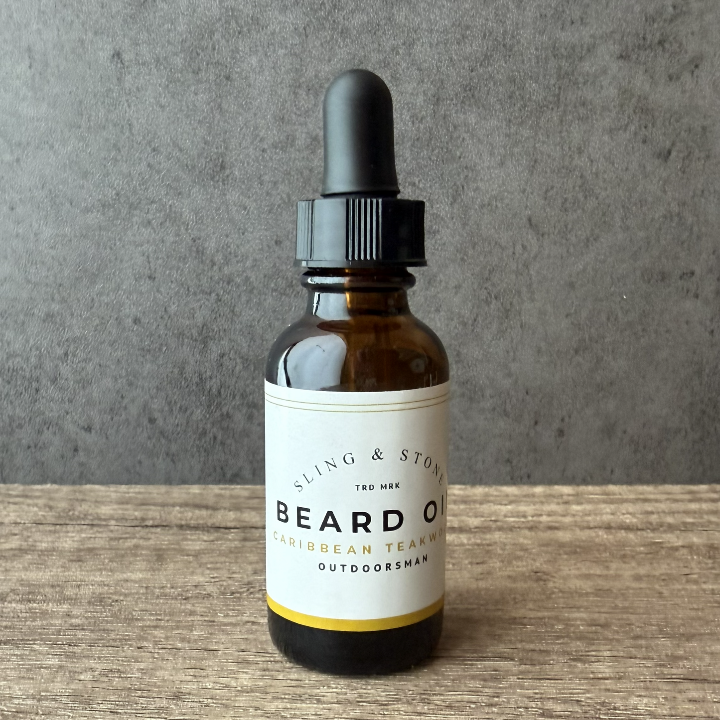 Bottle of Sling & Stone beard oil with dropper on a wooden surface and gray background