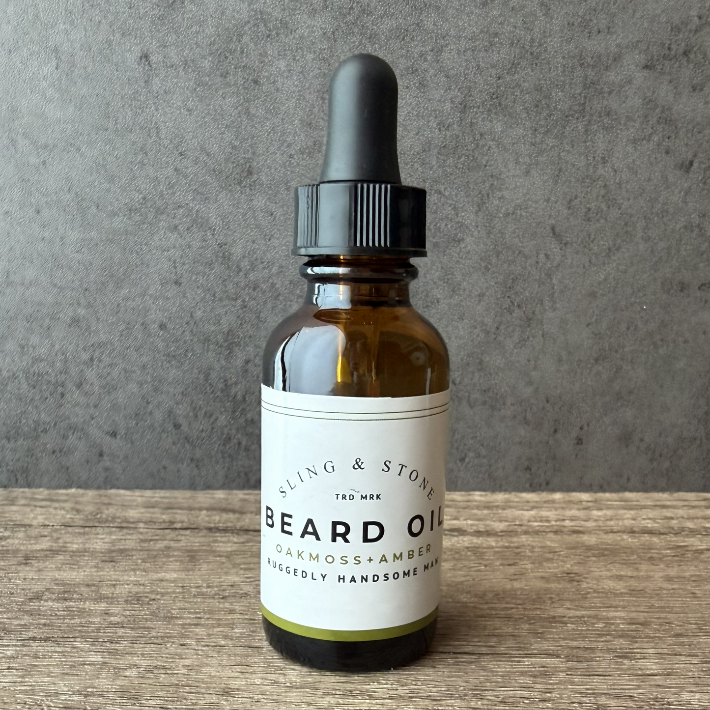 Bottle of Sling & Stone beard oil with dropper on a wooden surface and gray background