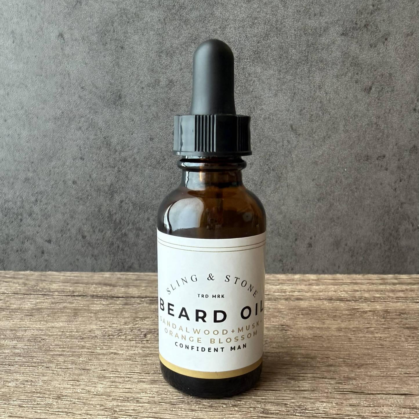 Bottle of Sling & Stone beard oil with dropper on a wooden surface and gray background