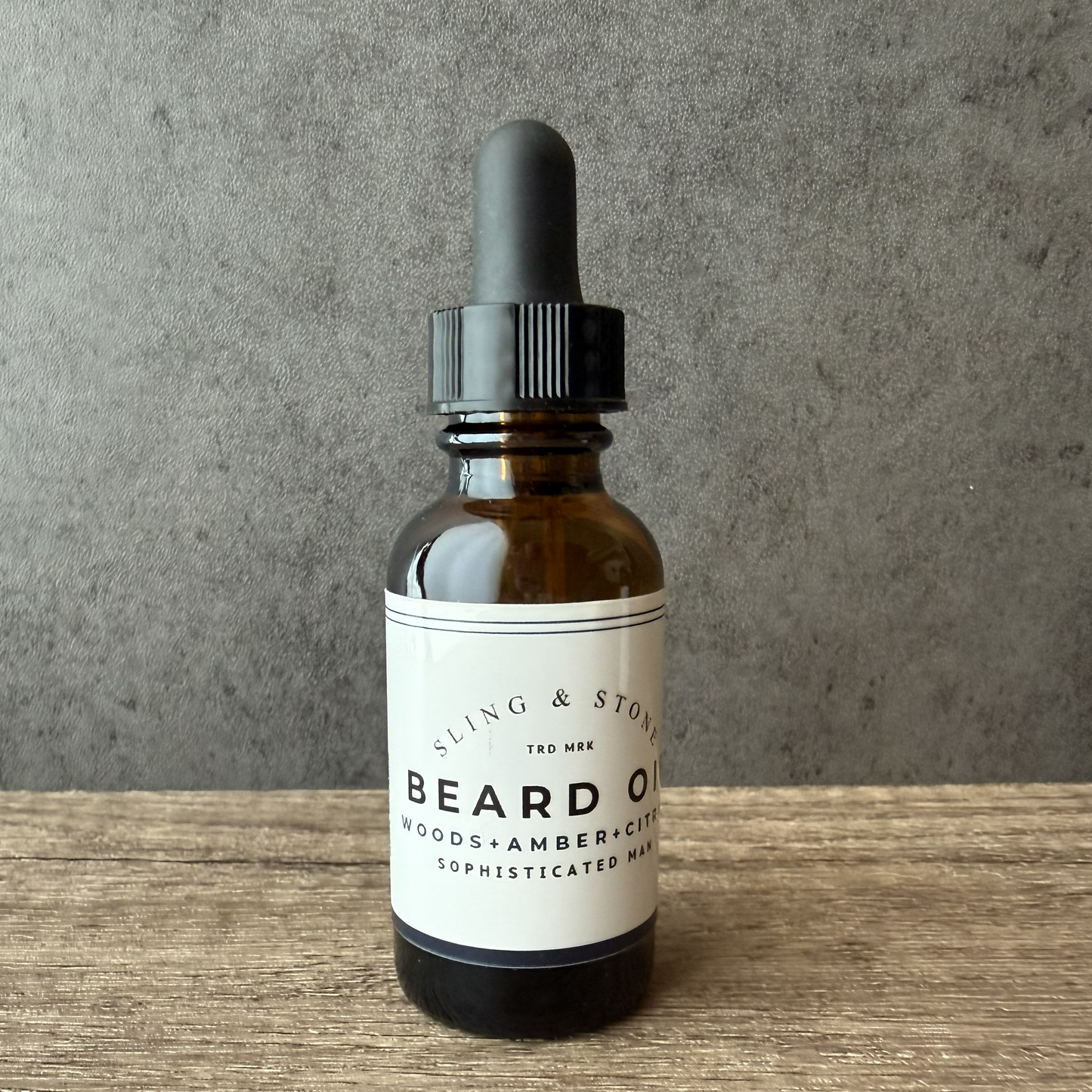 Bottle of sling & Stone beard oil with a dropper on a wooden surface and gray background
