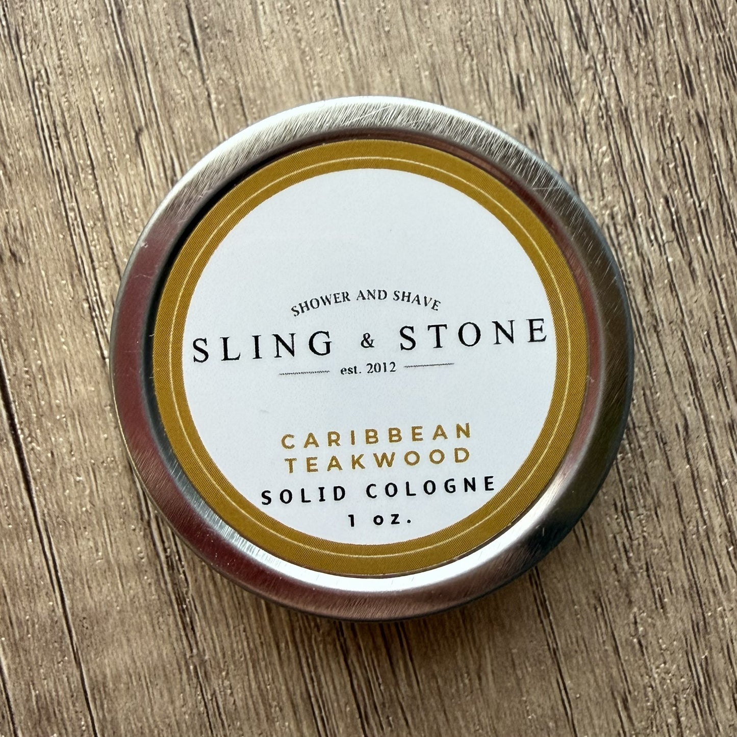Solid cologne container with 'Sling & Stone' branding on a wooden surface