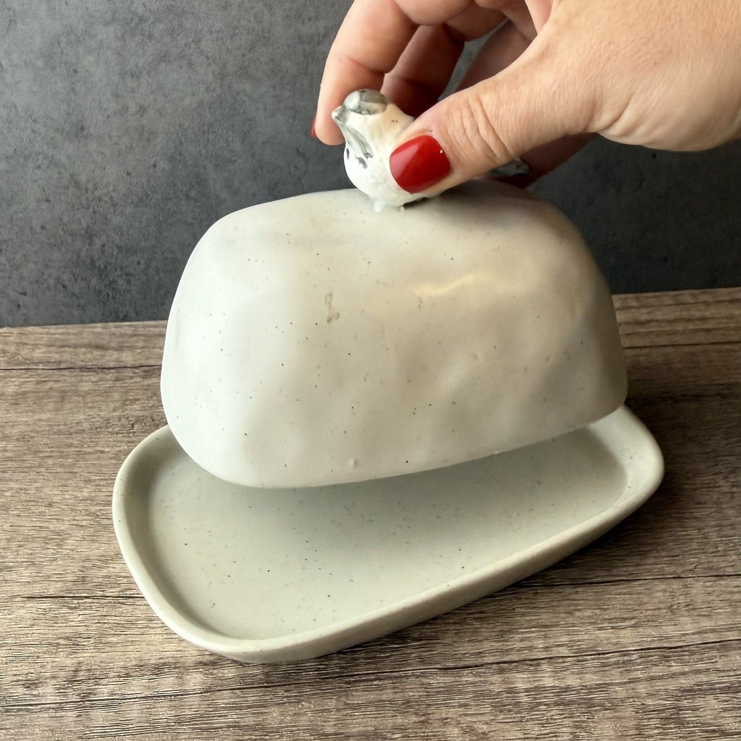 Person opening a white ceramic butter dish on a wooden surface