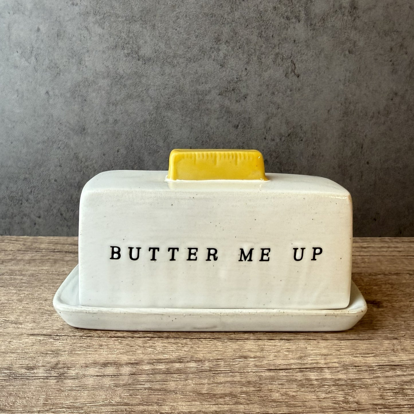 Butter dish with a yellow butter pat on a wooden surface and gray background