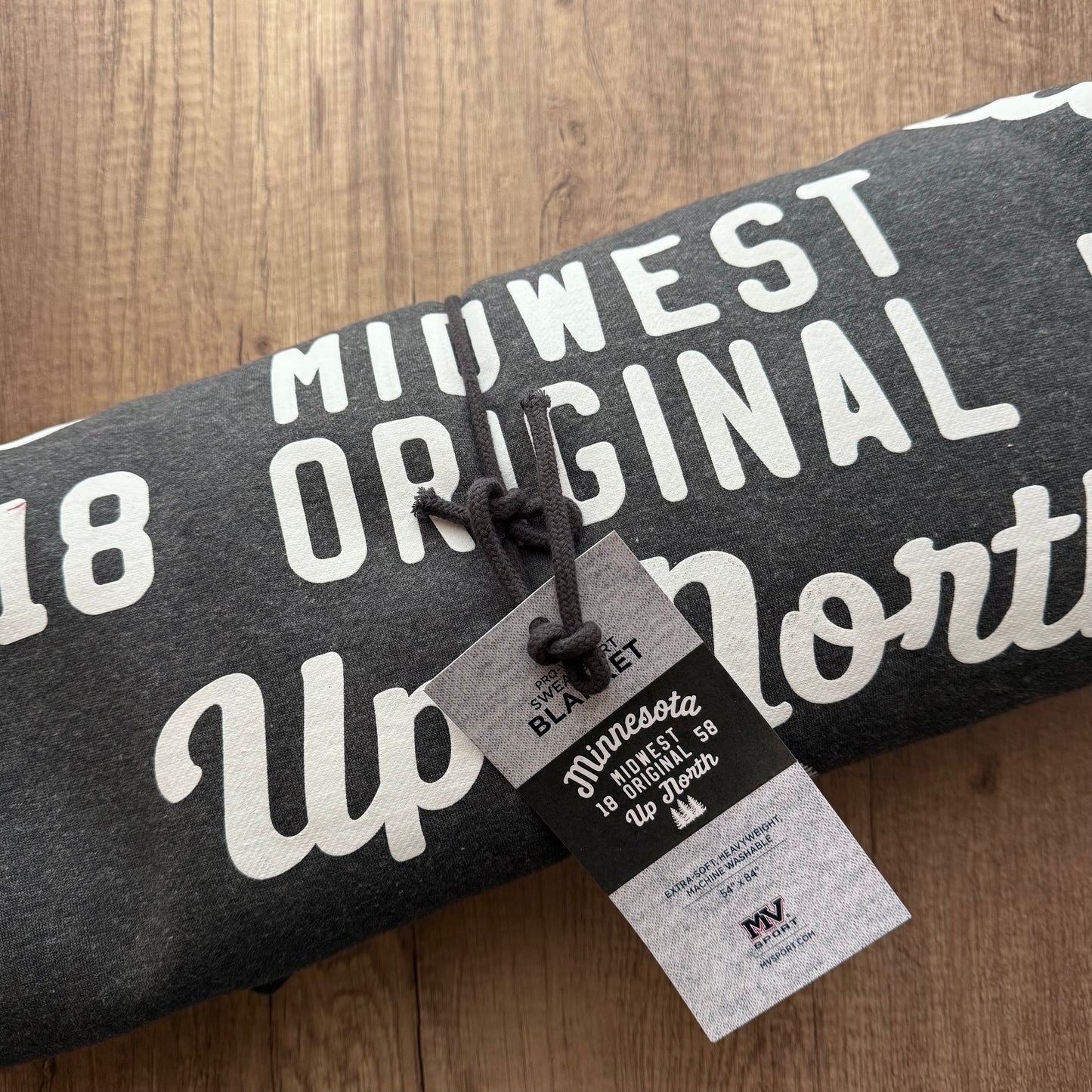 Gray sweatshirt with white text on a wooden surface, featuring a tag.
