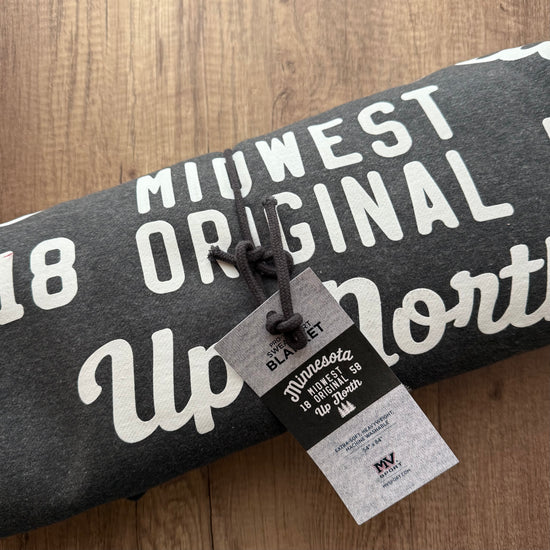 Gray sweatshirt with white text on a wooden surface, featuring a tag.