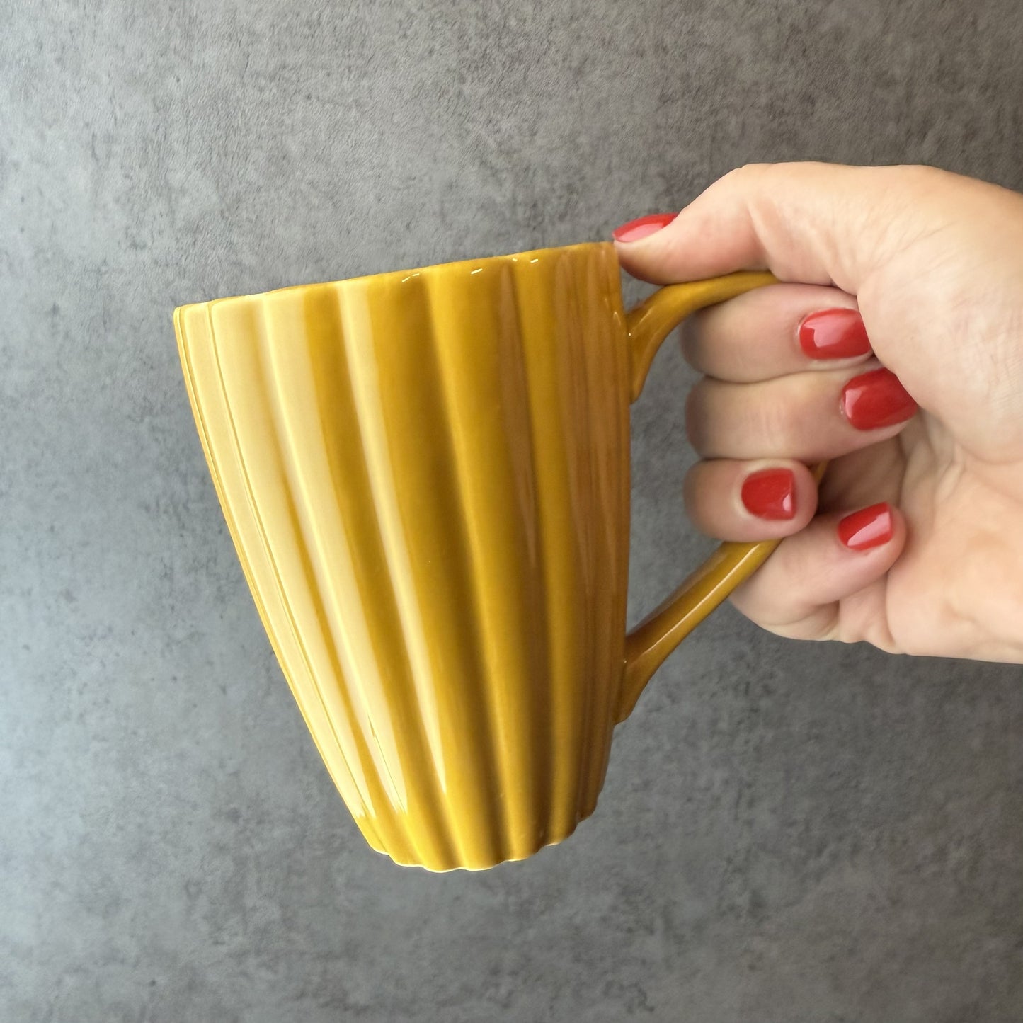 Hand holding a yellow mug against a gray background