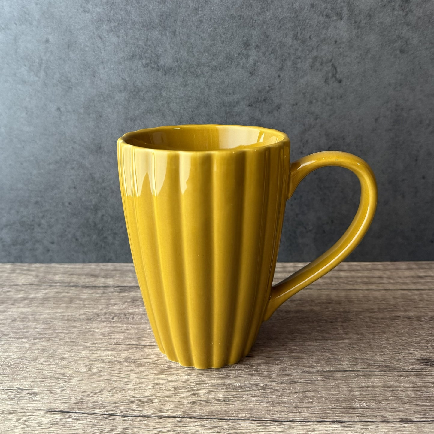 Yellow mug with ribbed texture on a wooden surface and gray background