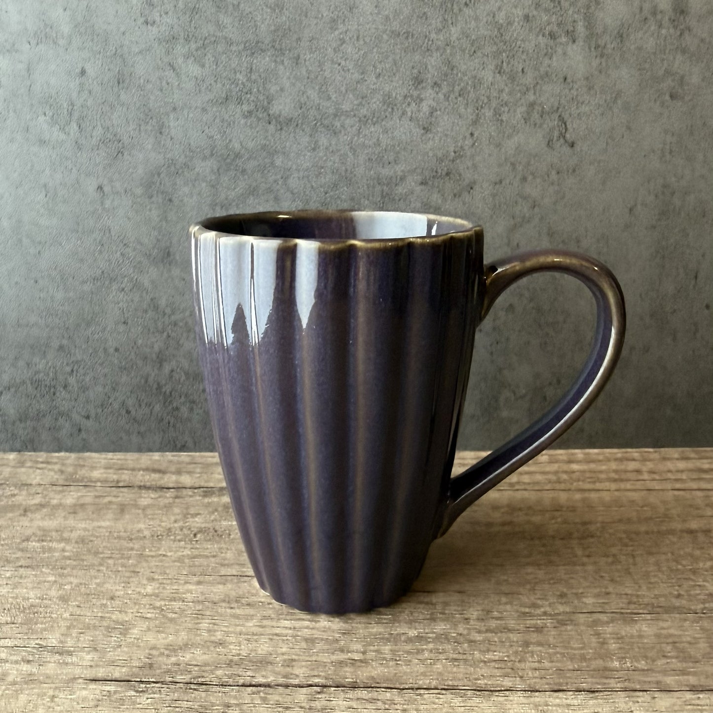Dark purple ceramic mug on a wooden surface with a gray background