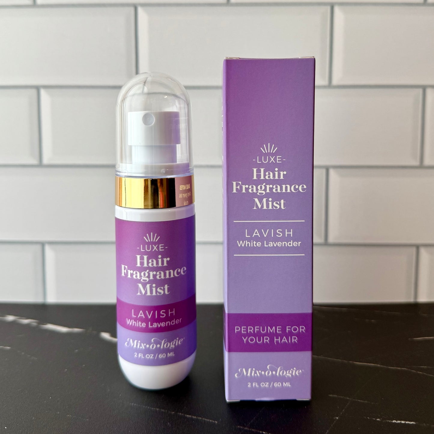 Hair fragrance mist bottle and packaging on a dark surface with a tiled wall background