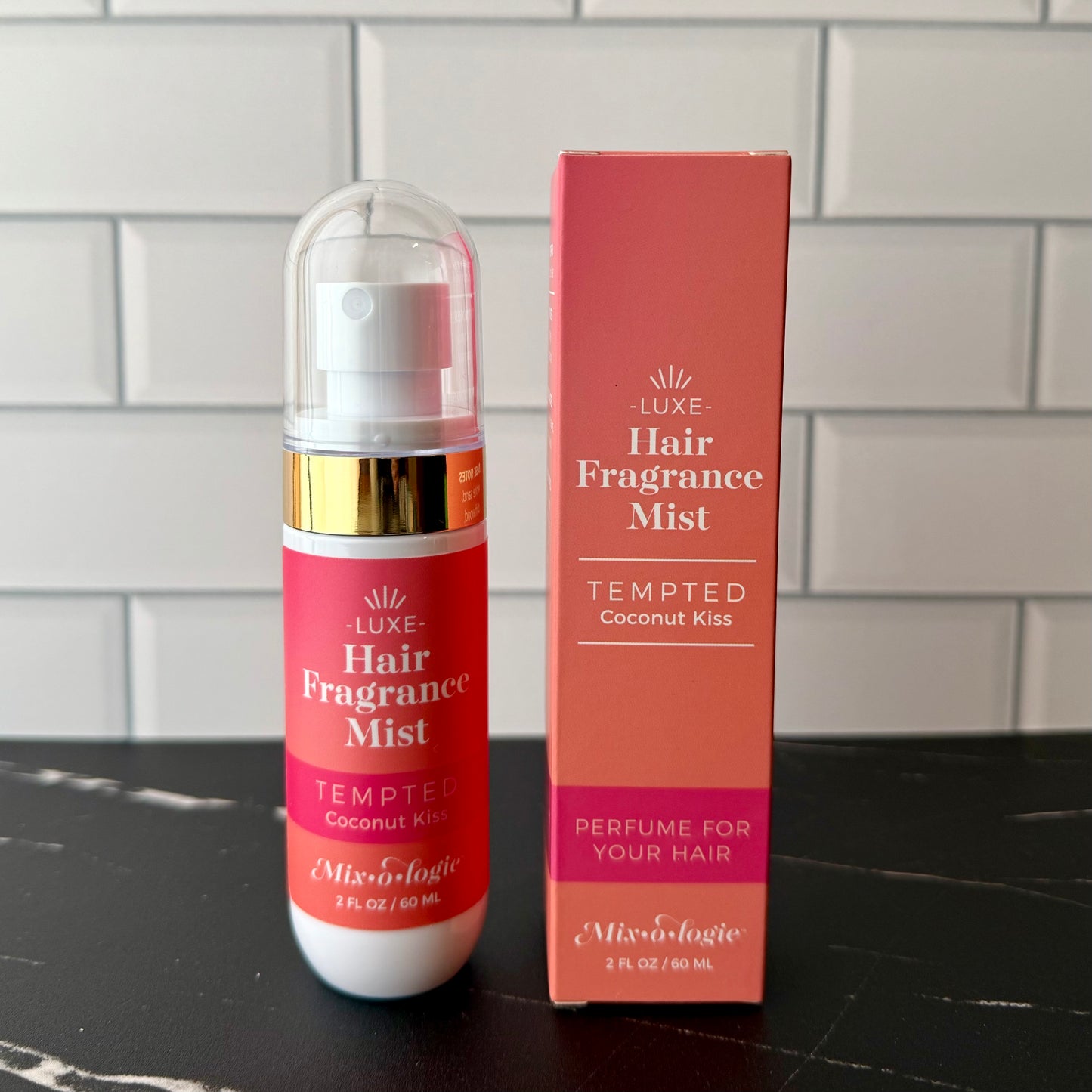 Red hair fragrance mist bottle and packaging on a black surface with a tiled wall background