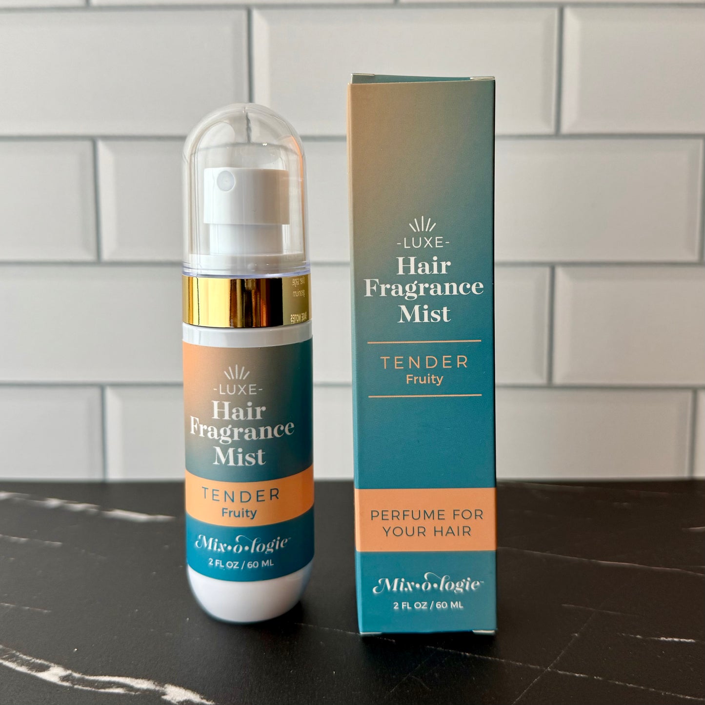 Hair fragrance mist bottle and packaging on a dark surface with a tiled wall background