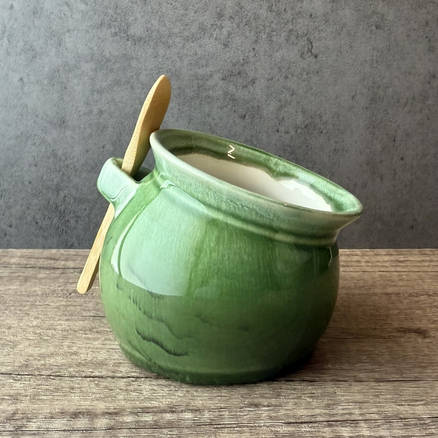 Green ceramic jar with a gold spoon on a wooden surface and gray background