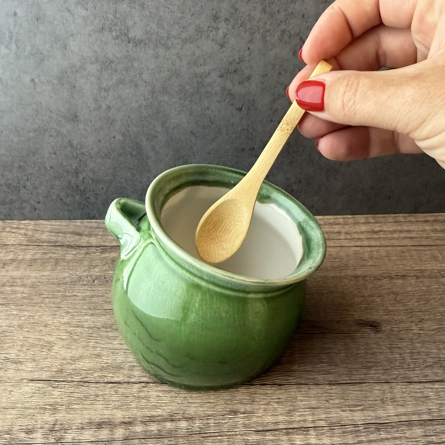 Green ceramic jar with a wooden spoon on a wooden surface