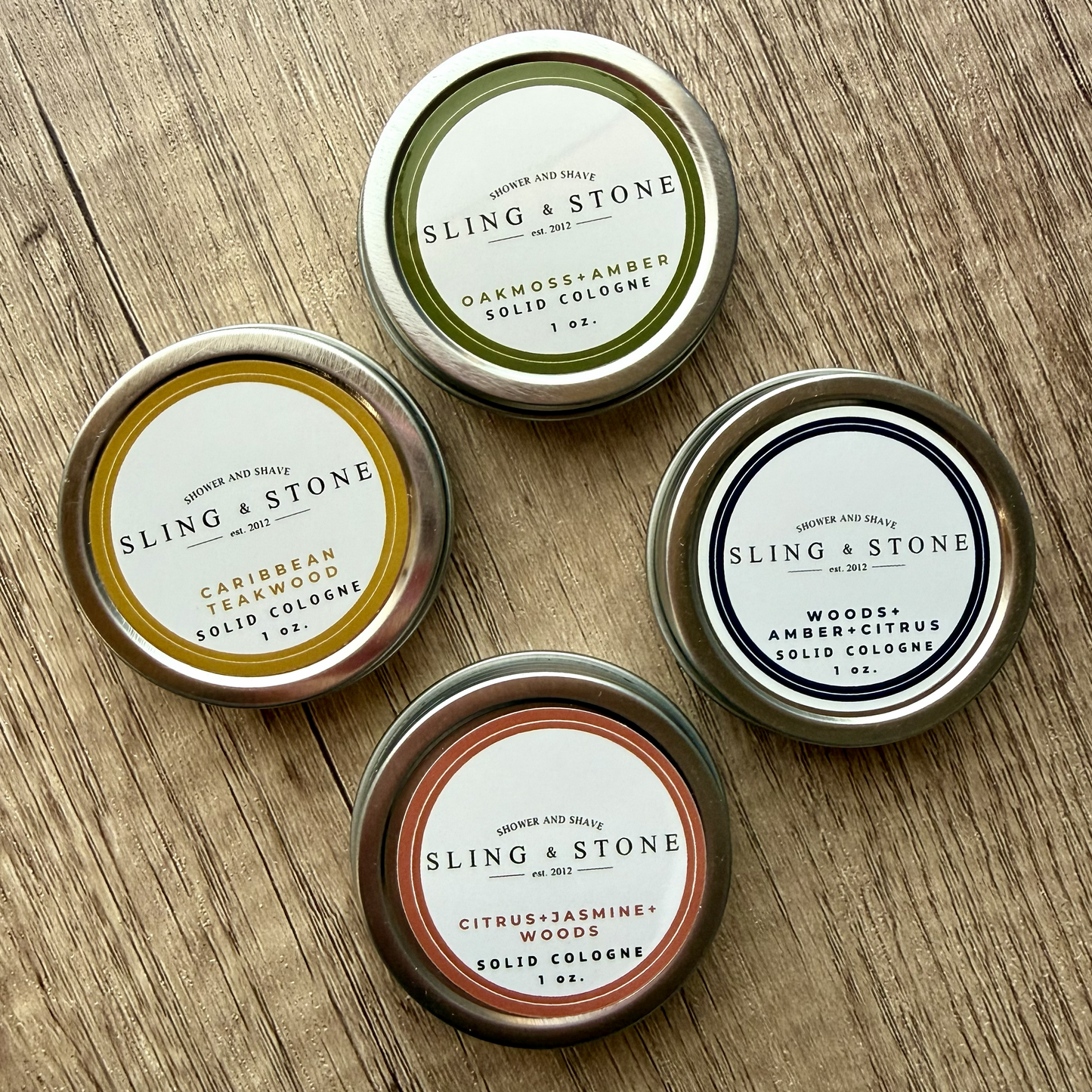 Four tins of Sling & Stone solid colognes on a wooden surface