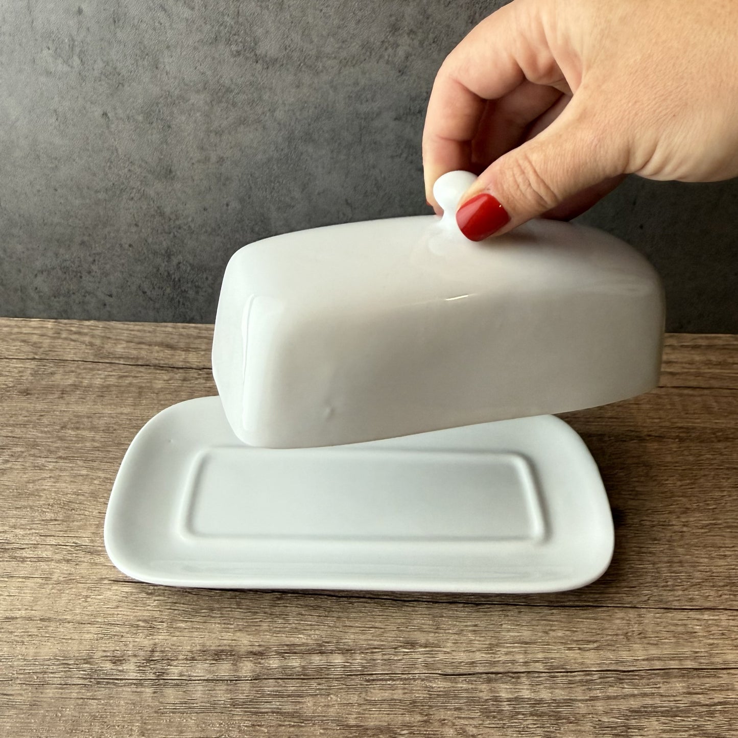 White ceramic butter dish with lid on a wooden surface against a gray wall.