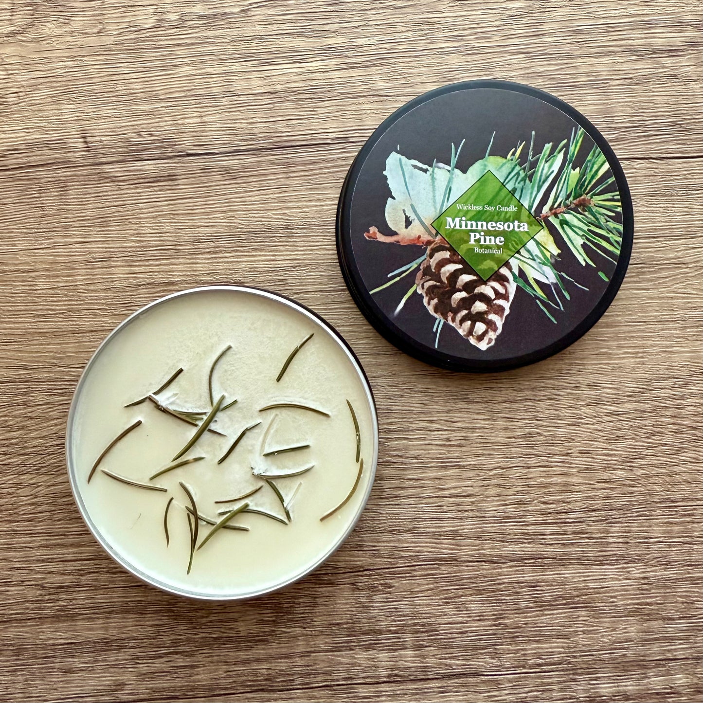 Candle in a tin with 'Minnesota Pine' lid on a wooden surface