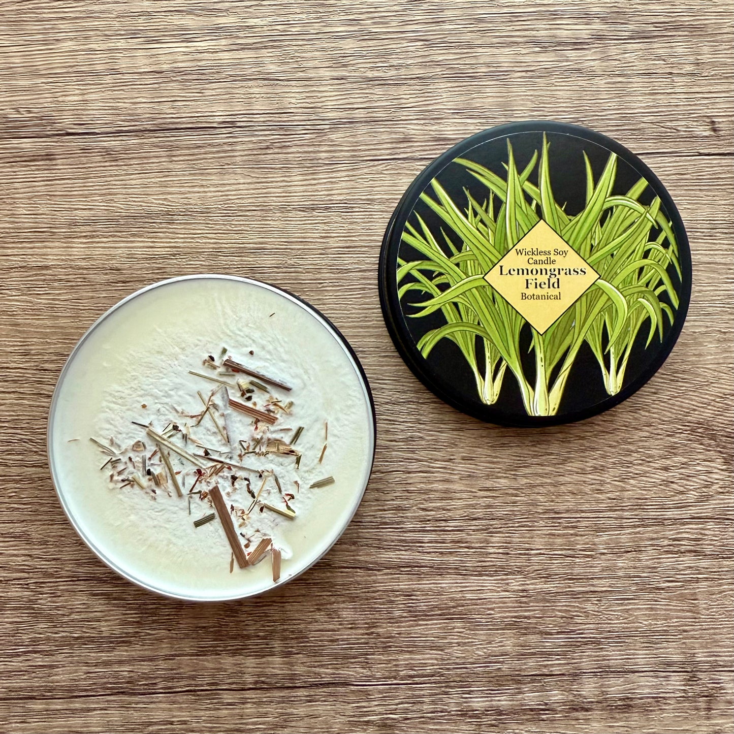 Two round containers on a wooden surface, one with a lid featuring lemongrass design.