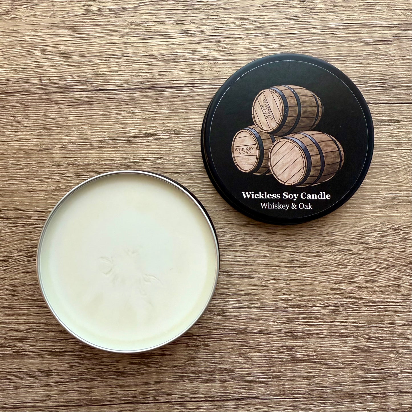 Wickless soy candle in a tin with a decorative lid on a wooden surface